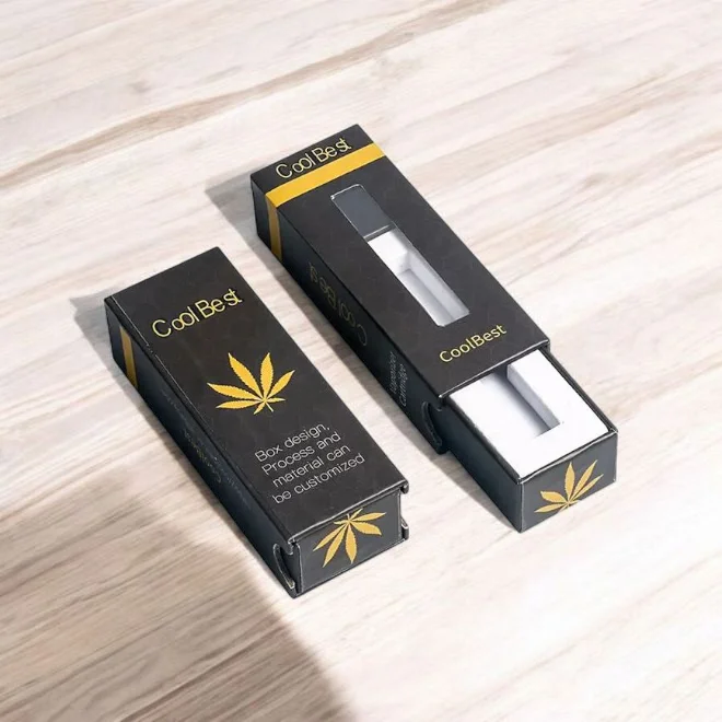 Black custom CBD e-cigarette boxes branded as "Cool Best" with gold cannabis leaf design and a clear window, displayed on a light wooden surface.