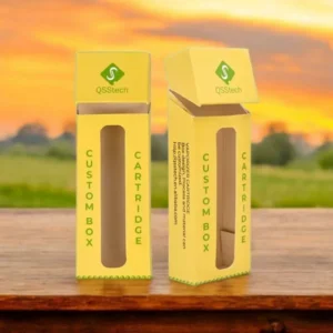 Custom yellow e-cigarette cartridge boxes with a clear window and flip-top lid, branded with QSSTech logo, placed on a wooden surface with a scenic sunset background.