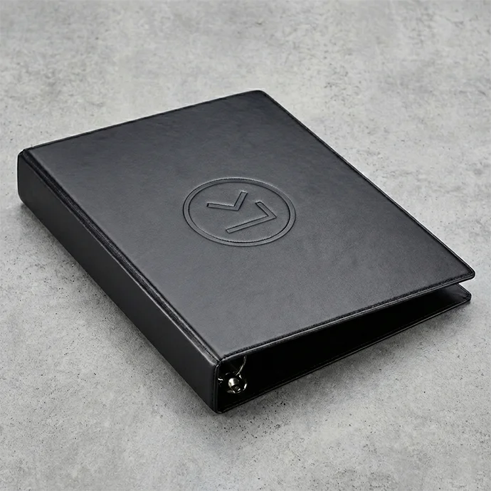 Black leather ring binder with a debossed circular logo on a grey textured surface